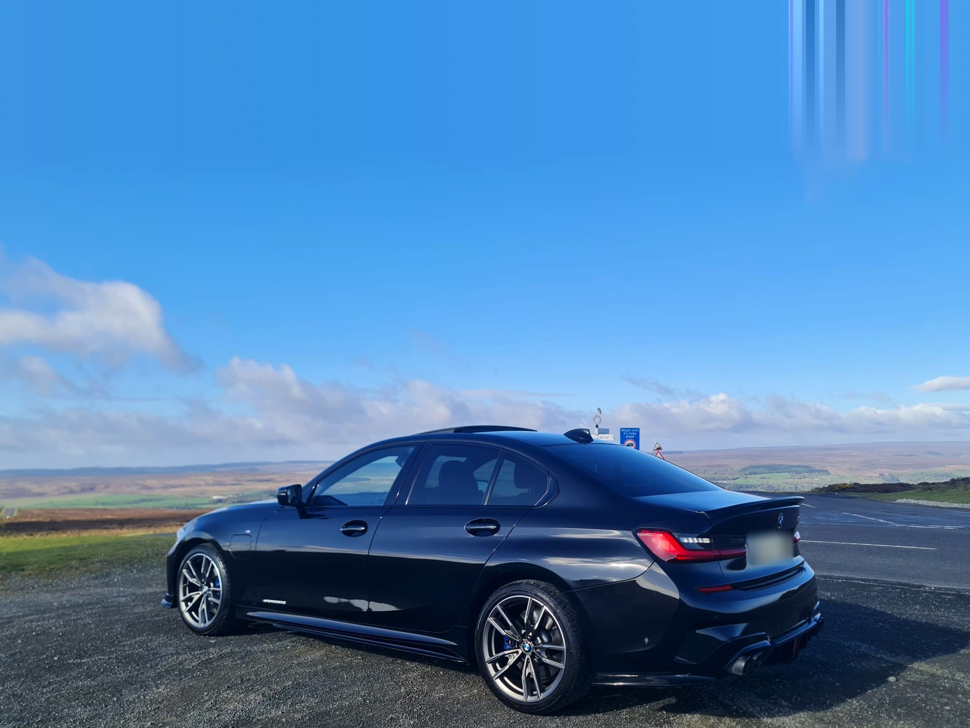 A black BMW 3 Series M Sport parked on a moorland pull-in, looking out over the valley